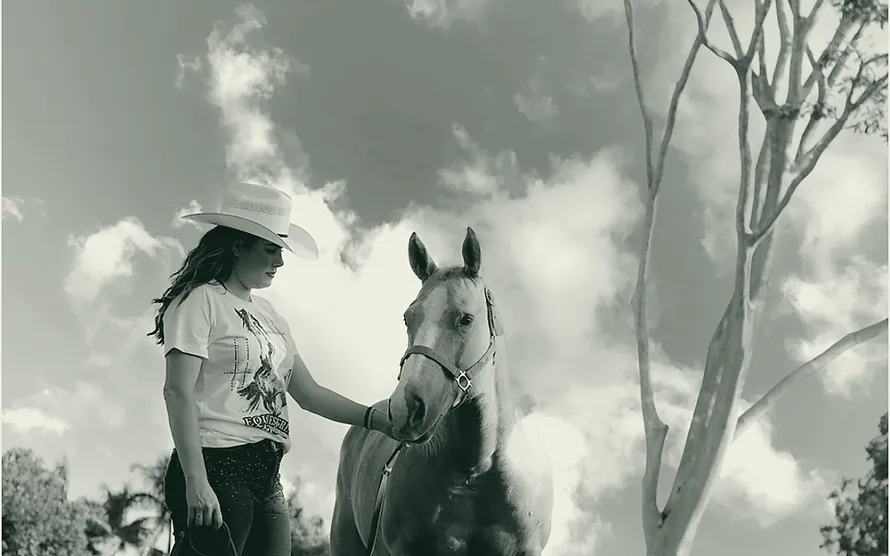 Uma mulher de chapéu ao lado de um cavalo palomino, com o céu aberto atrás